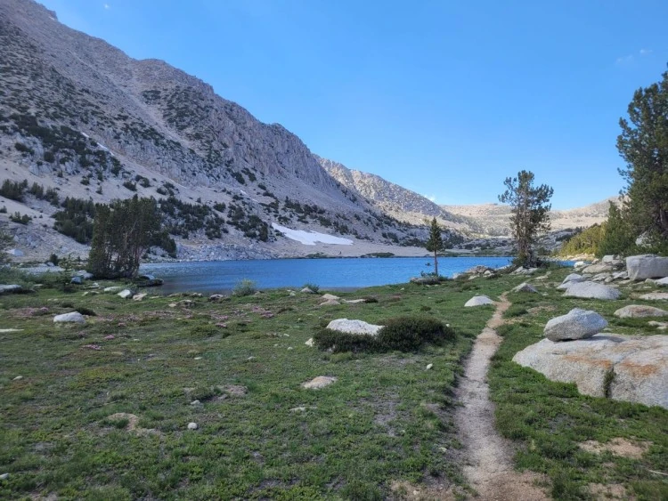 The trail reaches an alpine lake beneath granite slopes.